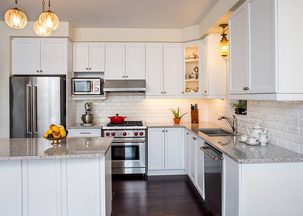 Modern white kitchen with stainless steel appliances, granite countertops, and bright lighting.